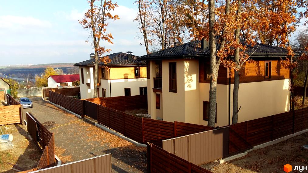 Котеджне містечко КМ Віта Паркова. Сучасні двоповерхові будинки з дерев'яними елементами фасаду та темним дахом. Огороджена територія з парканом та дорогою.