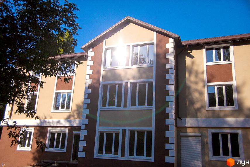 Зовнішній вигляд ЖК Дім на Набережній: триповерховий будинок з коричневими та бежевими фасадами, білими вікнами та декоративними елементами. Зелені дерева біля будівлі.