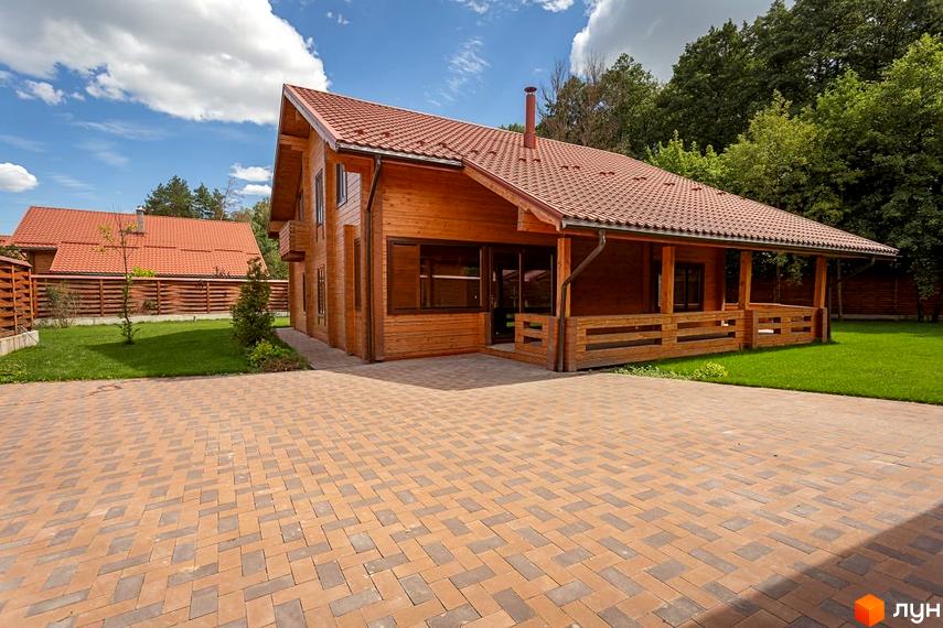 Двоповерховий дерев'яний будинок з червоним черепичним дахом та верандою. Навколо будинку доглянутий газон та вимощена бруківкою територія.