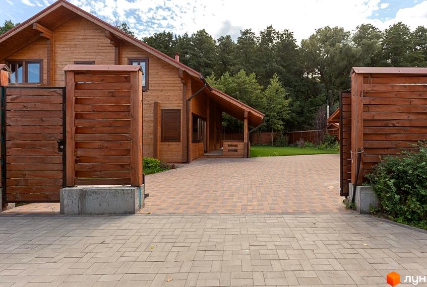 Котеджне містечко Summerville: дерев'яний будинок з навісом та вимощеним подвір'ям. Територія оточена дерев'яним парканом.