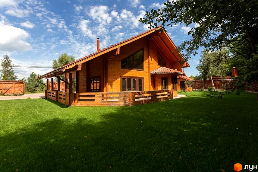 Котеджне містечко Summerville: дерев'яний будинок з терасою та зеленим газоном. Навколо будинку розташована доглянута прибудинкова територія з парканом та деревами.