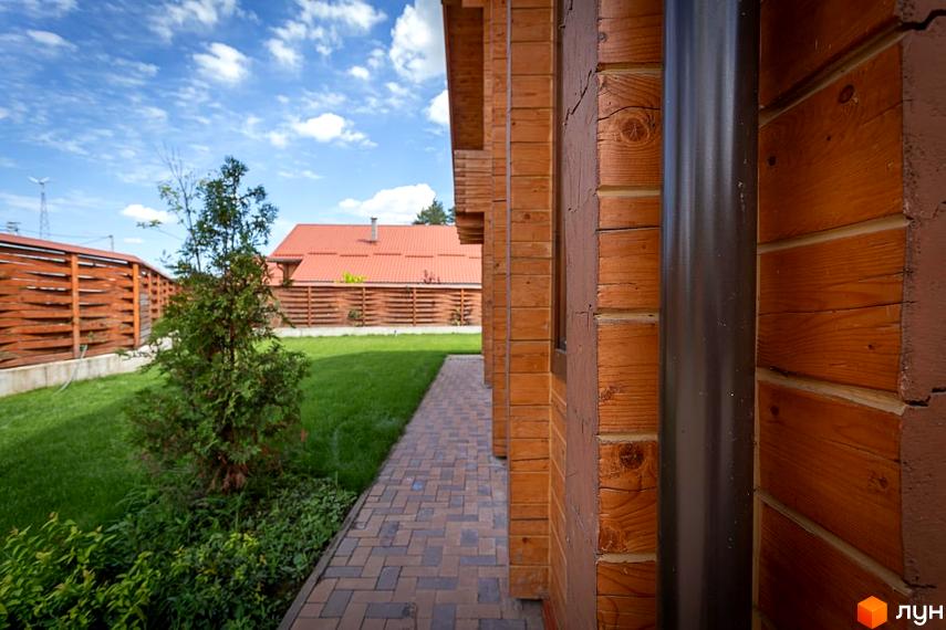 Зовнішній вигляд будинку з дерев'яних брусів у котеджному містечку КМ Summerville. Прибудинкова територія з зеленим газоном та доріжкою з плитки.