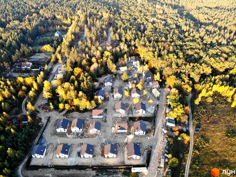 Котеджне містечко Ліс та Озеро: вид згори на нові будинки з коричневими та сірими дахами, розташовані серед осіннього лісу. Навколо будинків видно будівельні роботи та дороги.