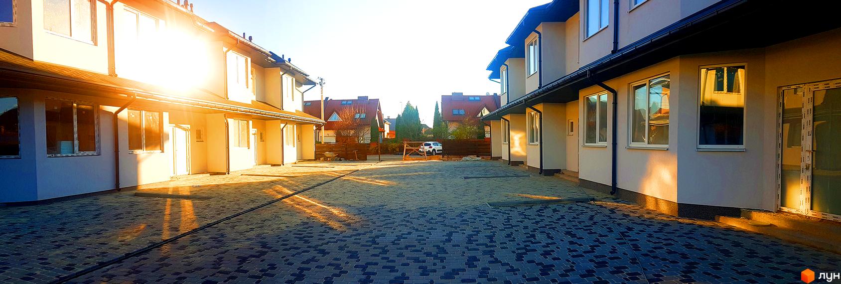 Зображення фасаду таунхаусів житлового комплексу New Town. Видно бруківку перед будинками та сонячне світло, що освітлює територію.