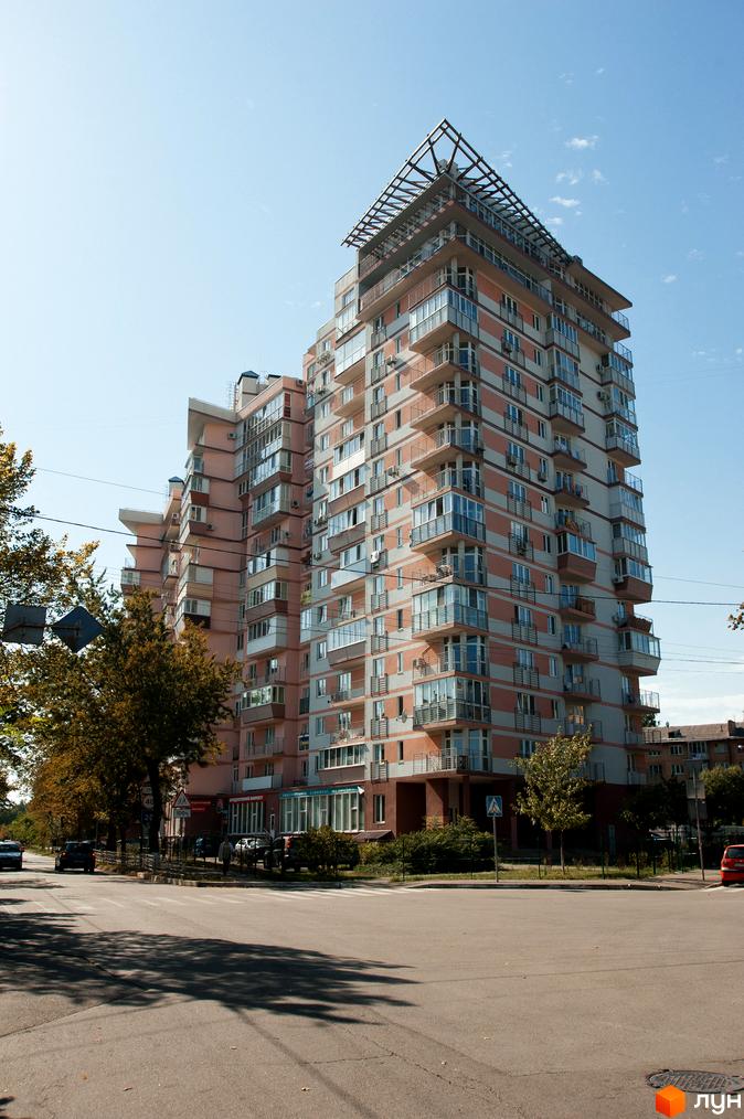 Житловий комплекс на вул. Януша Корчака, 25. Вид на будинок з балконами та прибудинковою територією з зеленими насадженнями.