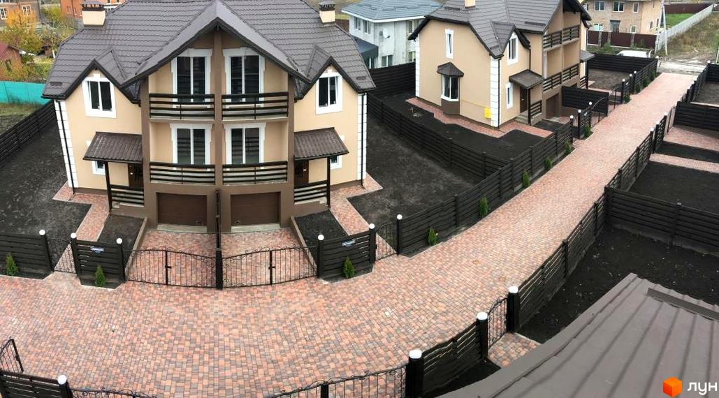 Зовнішній вигляд дуплексів Cottage Residence з коричневими дахами та бежевими стінами. Прибудинкова територія з бруківкою та парканом.