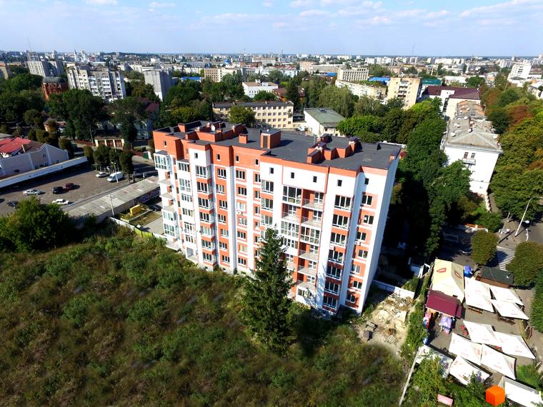 Висотна новобудова ЖК Сіті Парк з біло-оранжевим фасадом. Навколо будинку зелені насадження та міська забудова.