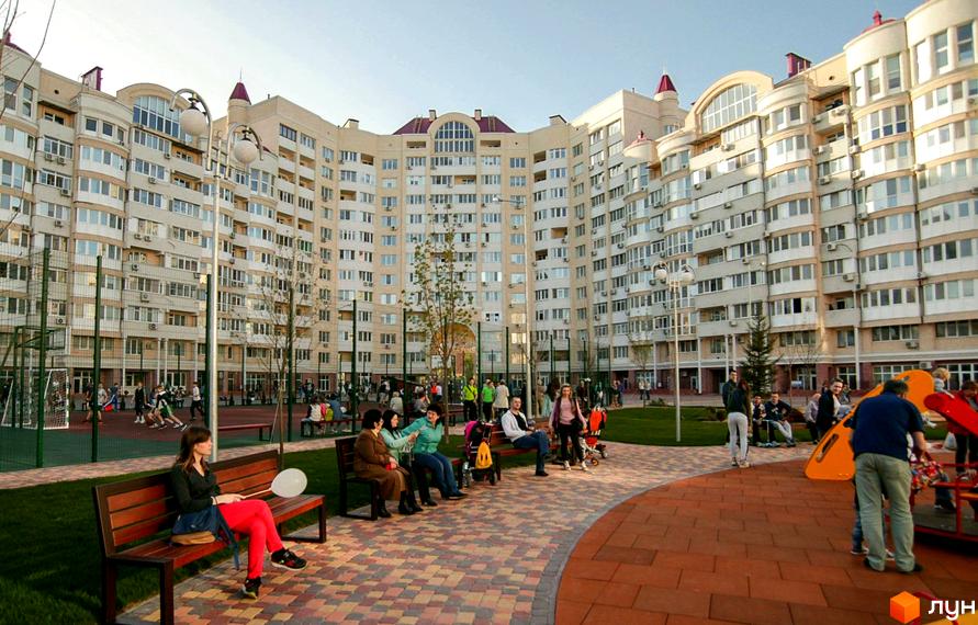 Житловий комплекс Рів'єра. Великий житловий будинок з вигнутим фасадом та численними балконами. Прибудинкова територія з лавочками, дитячим майданчиком та спортивною зоною.