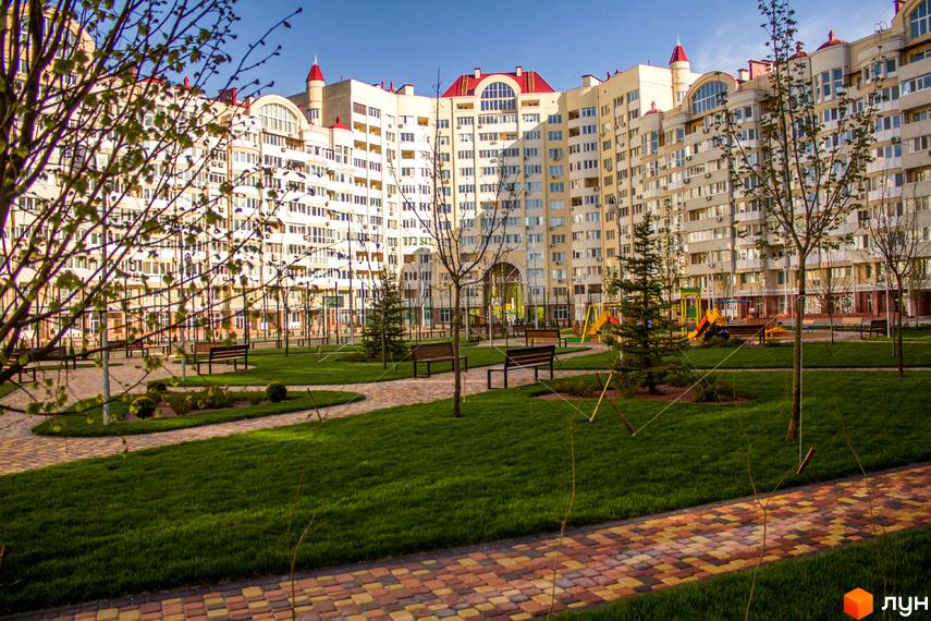 Житловий комплекс Рів'єра з вигнутими фасадами та червоними дахами. На прибудинковій території зелений газон, доріжки та лавки.