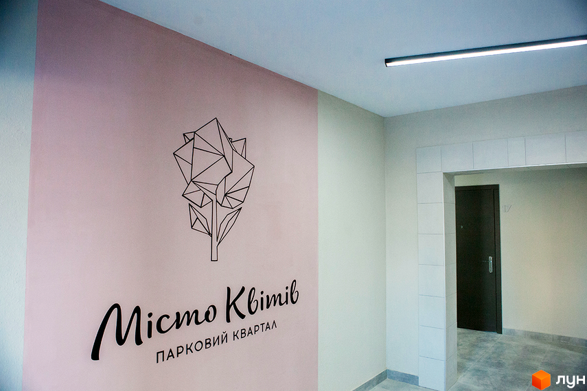 Зображення фасаду житлового комплексу Місто Квітів. Парковий квартал. На стіні нанесено логотип та назву комплексу. Вхід до під'їзду оформлений плиткою.