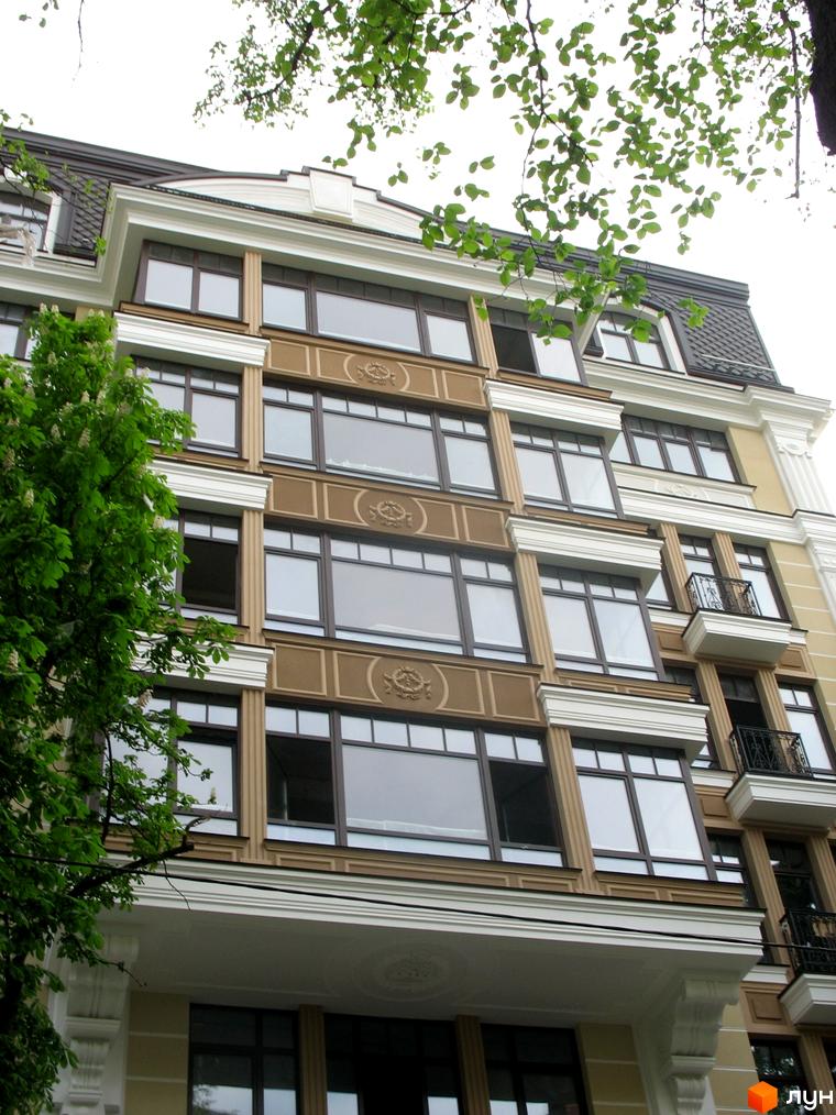 Фасад житлового комплексу на вул. Десятинна, 11 з великими вікнами та архітектурними елементами. Прибудинкова територія з зеленими насадженнями.