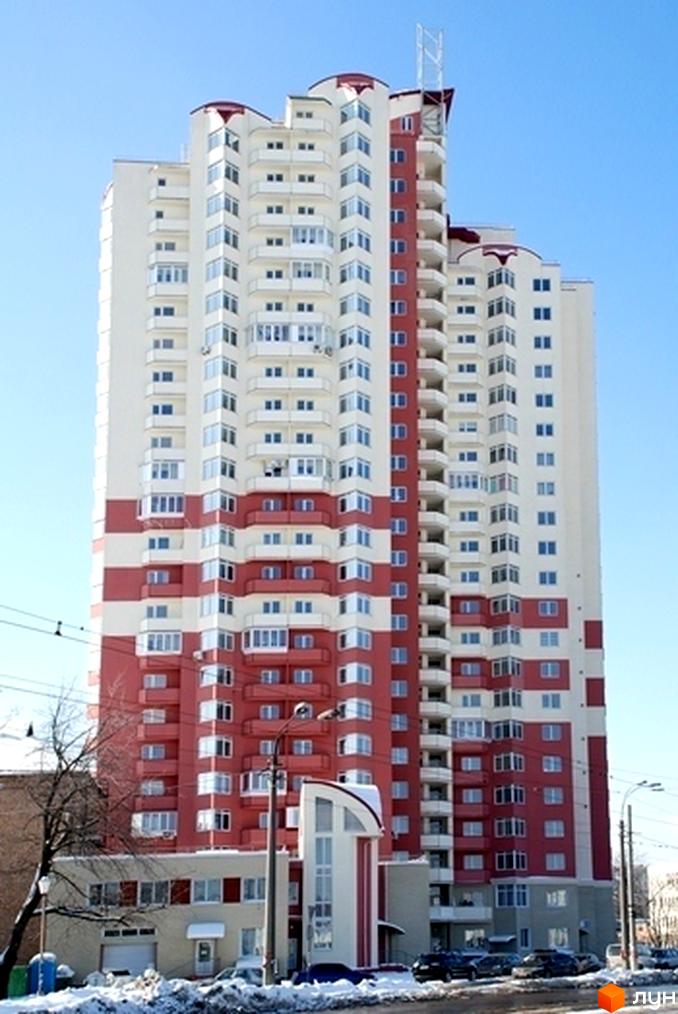 Багатоповерховий житловий комплекс Санаторний з біло-червоним фасадом та численними балконами. Навколо будівлі засніжена територія з припаркованими автомобілями.