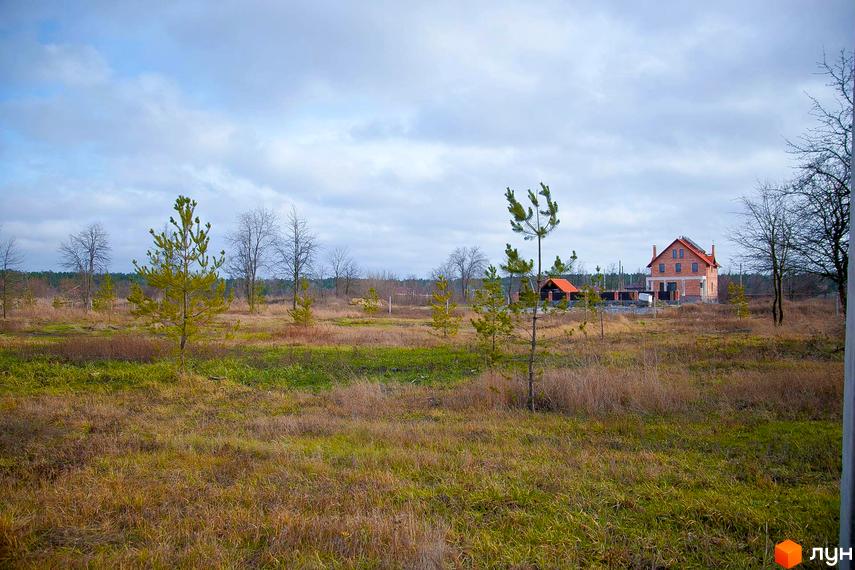 Вигляд на двоповерховий будинок з червоної цегли в Котеджному містечку Лісова Пристань. Навколо будинку зелена трава та дерева.