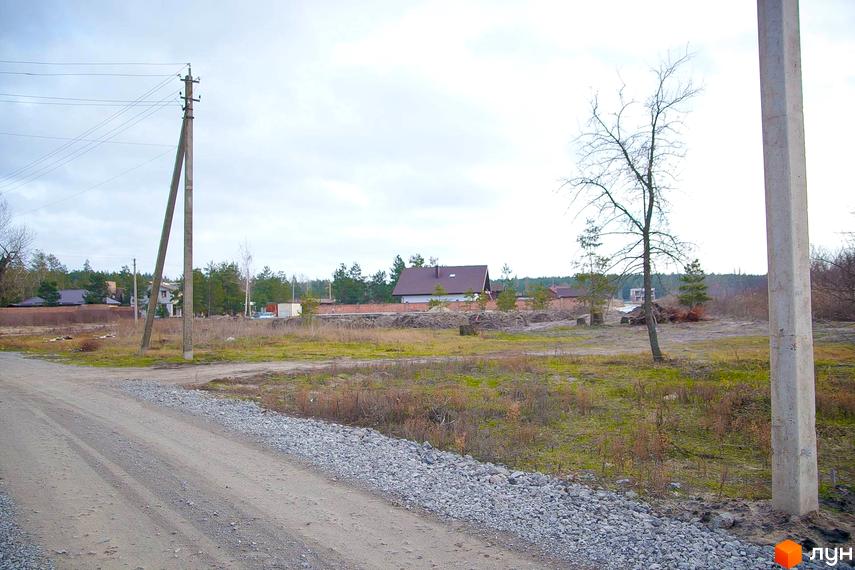 Вигляд на Котеджне містечко Лісова Пристань з дорогою та лініями електропередач. На задньому плані видно будинок з коричневим дахом.
