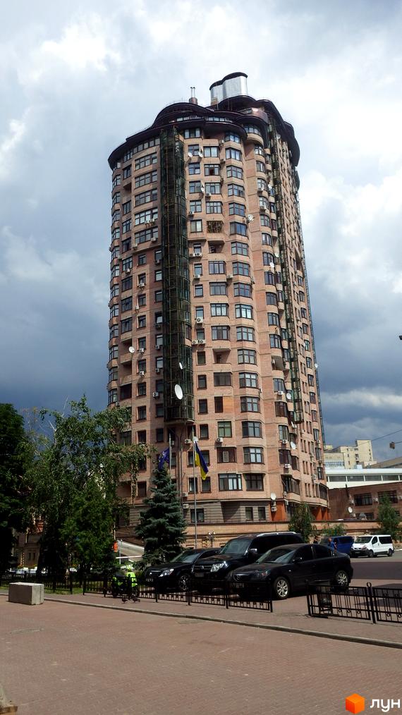 Житловий комплекс на вул. Євгена Коновальця, 36в, з фасадом з червоної цегли та великими вікнами. Прибудинкова територія з зеленими насадженнями та парковкою.