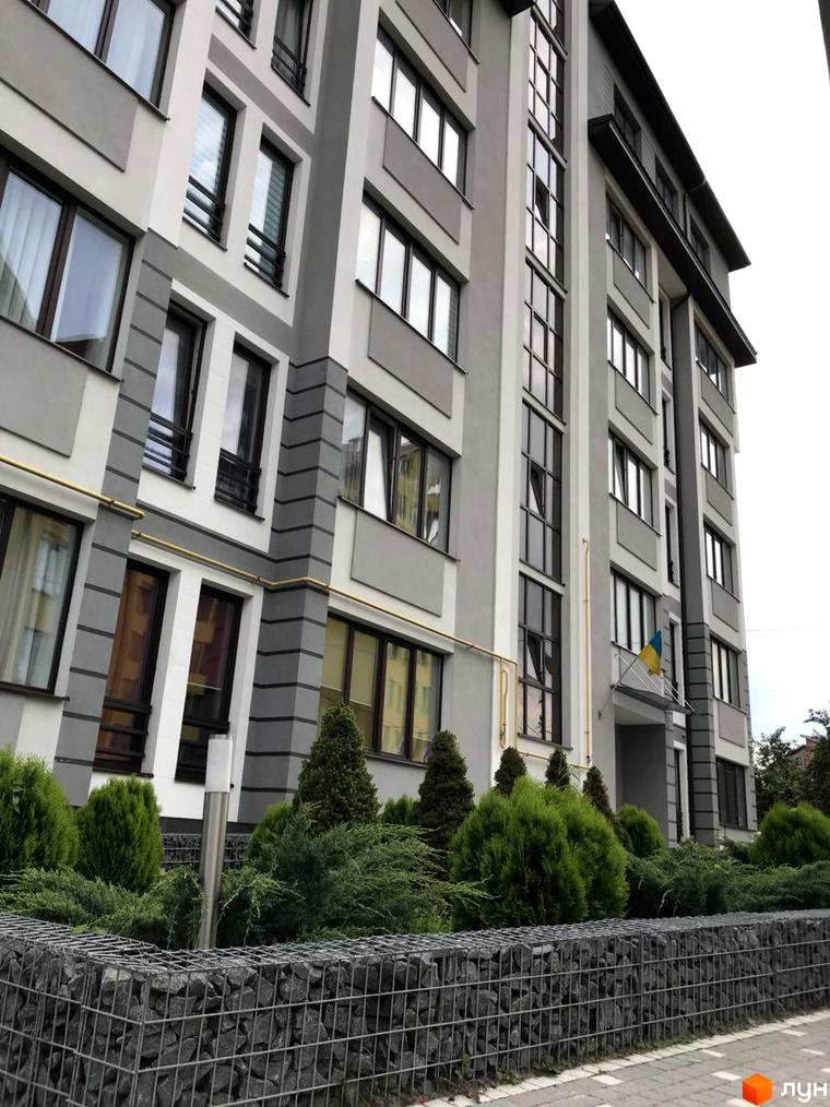 Зовнішній вигляд багатоповерхового будинку в Житловому районі Срібний Дім Преміум. На передньому плані декоративні кущі та кам'яна огорожа.