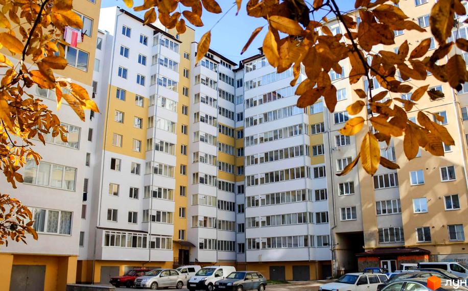 Житловий комплекс на вул. Галицька, 118в, з фасадом жовто-білого кольору та прибудинковою територією з автомобілями.