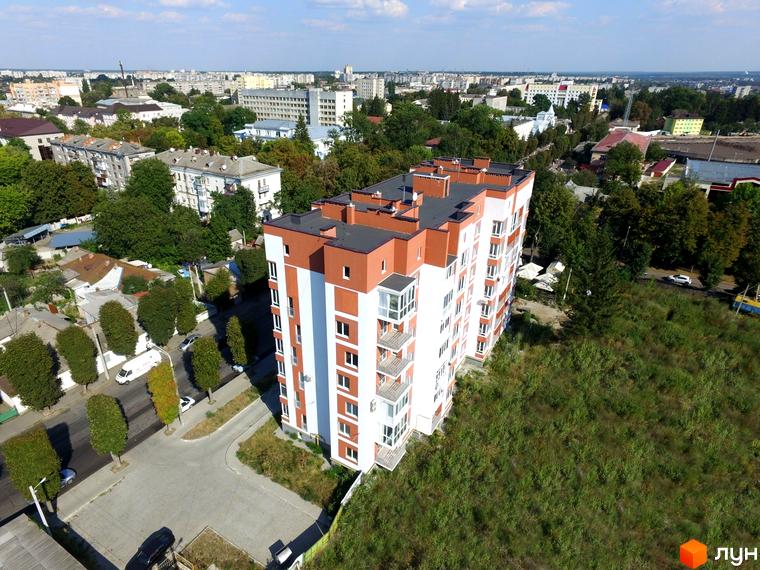 Висотна новобудова ЖК Сіті Парк з білими та коричневими фасадами на тлі міської забудови. Поруч зелені насадження та асфальтована дорога.