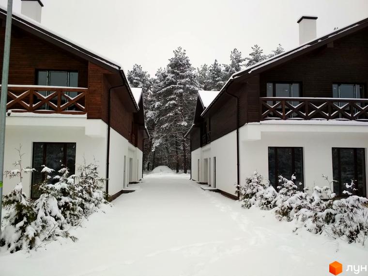 Котеджне містечко Bruhsell: двоповерхові будинки з дерев'яним оздобленням та білим фасадом на тлі зимового лісу. Засніжена територія навколо.