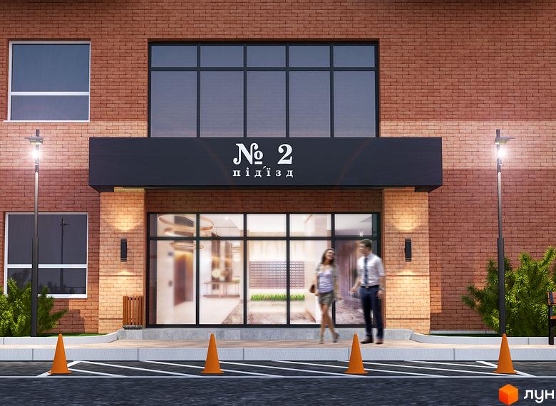 Вхідна група будинку ЖК Авіатор з цегляною кладкою, панорамним склінням та ліхтарями. На передньому плані помаранчеві конуси та парковка.