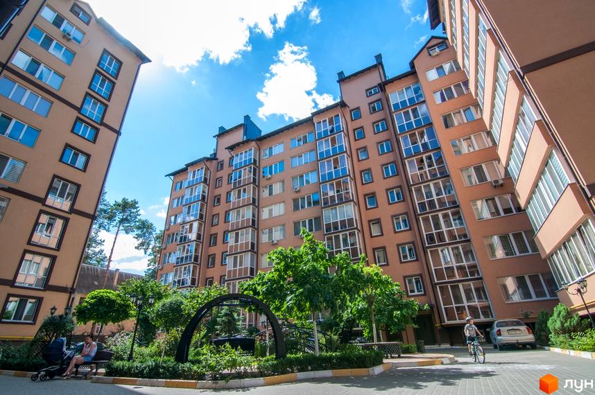 Житловий комплекс Полтавський двір. Високі будинки з великою кількістю вікон. На території комплексу є зелені насадження та місце для відпочинку.