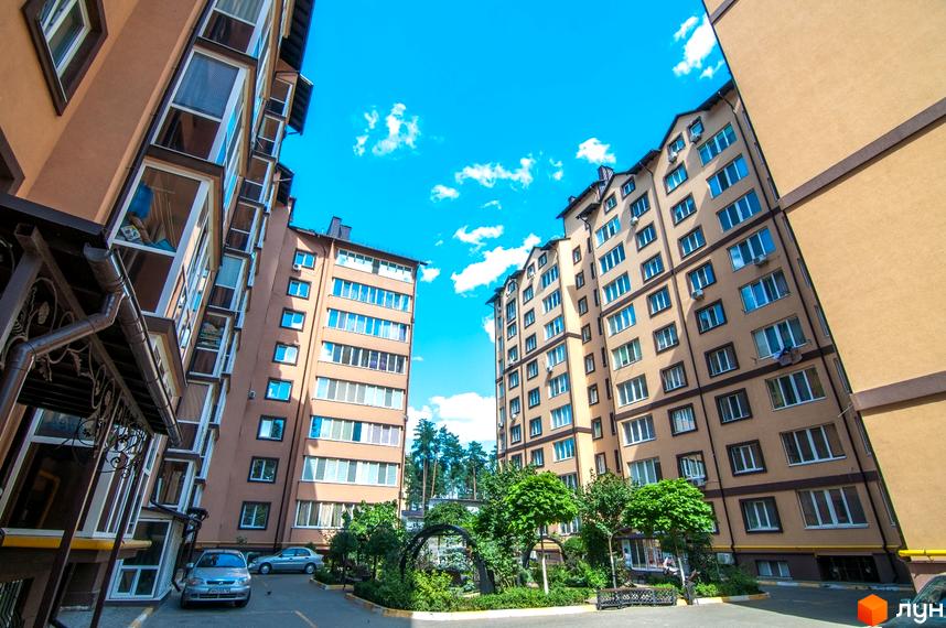 Житловий комплекс Полтавський двір з висотними будинками пісочного кольору на тлі блакитного неба. На території комплексу є зелені насадження та місця для відпочинку.