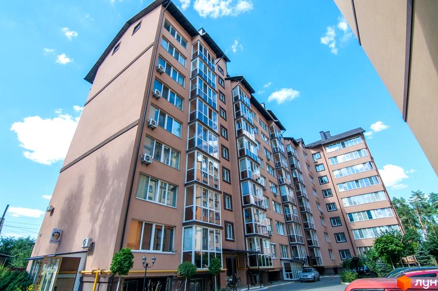 Високий будинок ЖК Полтавський двір з великою кількістю вікон на тлі блакитного неба. На прибудинковій території припарковані автомобілі та ростуть дерева.