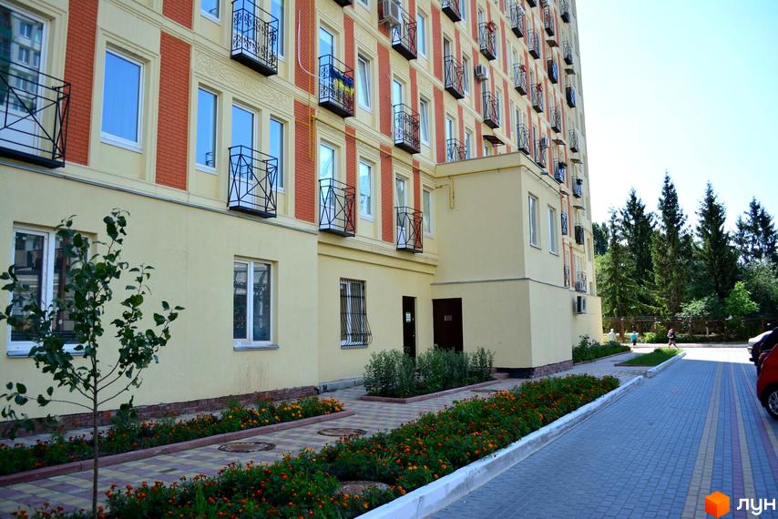 Житловий комплекс ЖК Грюнвальд - фасади будівель з червоною цеглою та жовтими елементами, балконами та кондиціонерами. Прибудинкова територія з квітами та доріжками.
