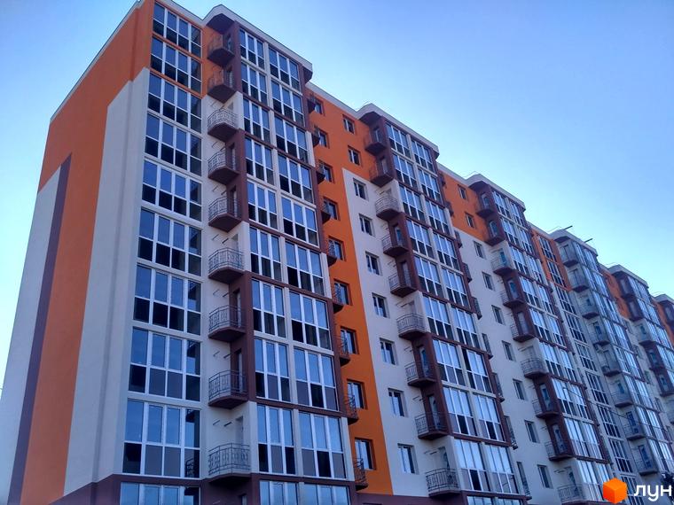Будинок житлового комплексу Громадянський посад з панорамними вікнами та балконами на тлі блакитного неба. Зовнішній вигляд новобудови з помаранчевими та білими фасадами.