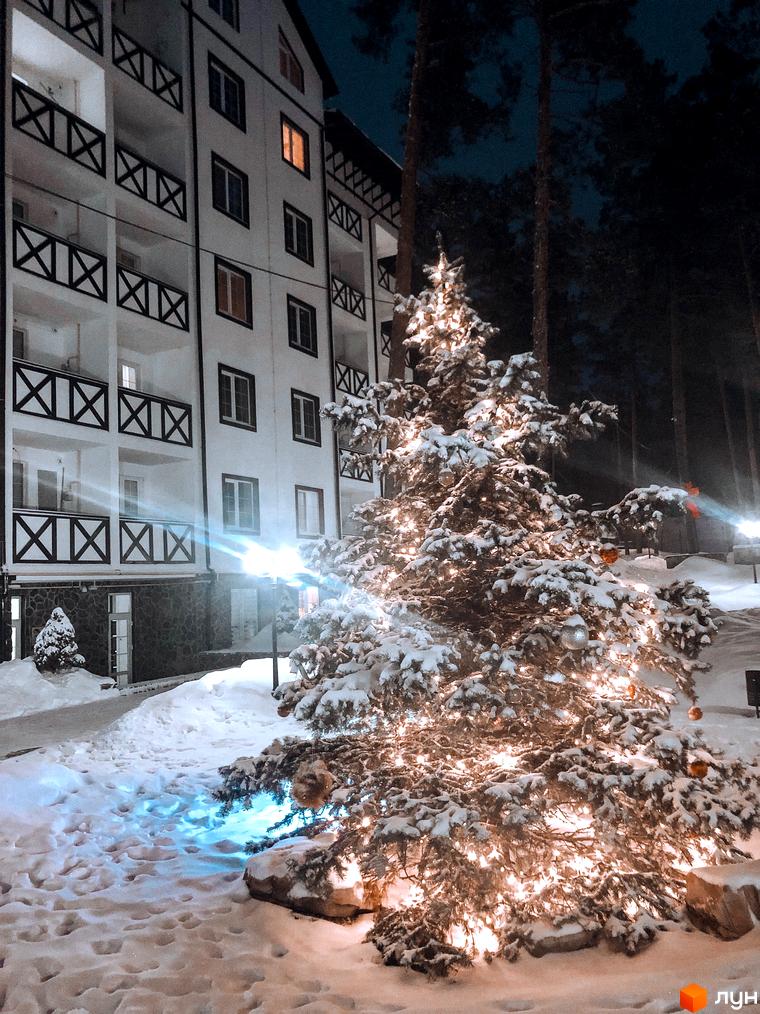 Житловий комплекс DESNA residence взимку, з новорічною ялинкою, прикрашеною гірляндами, на тлі багатоповерхового будинку. Навколо багато снігу.
