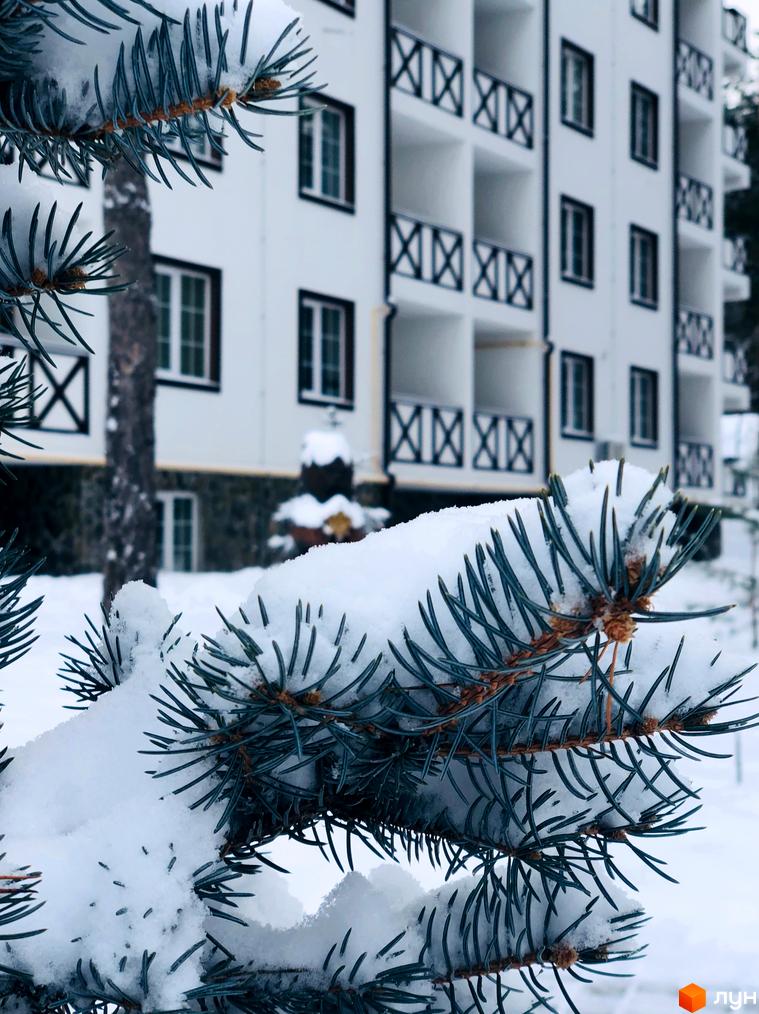 Житловий комплекс DESNA residence взимку. Біла багатоповерхівка з балконами та вікнами на тлі засніженої ялинки.