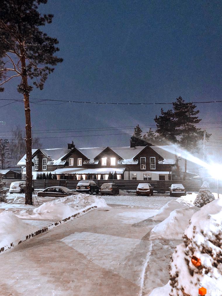 Таунхаус „Desna Residence“ взимку, з освітленими вікнами та засніженою територією. Парковка біля будинку, оточена снігом та деревами.