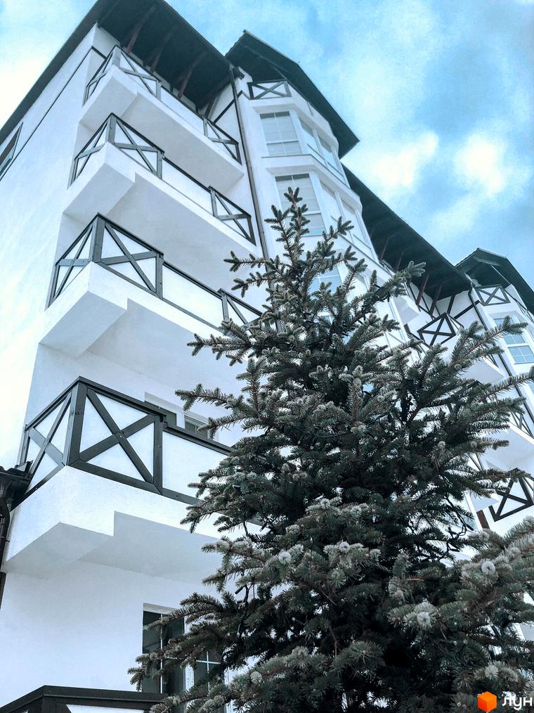 Житловий комплекс DESNA residence: біла багатоповерхова будівля з балконами та темними дерев'яними елементами фасаду, поруч зелена ялина.