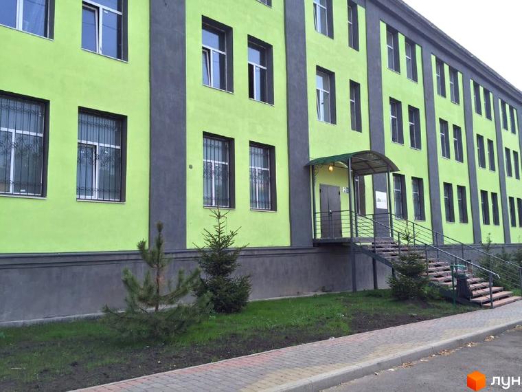 Зображення фасаду будівлі Житлового комплексу Green park з зеленими стінами та темними вікнами. Перед будинком розташована доглянута прибудинкова територія з деревами.