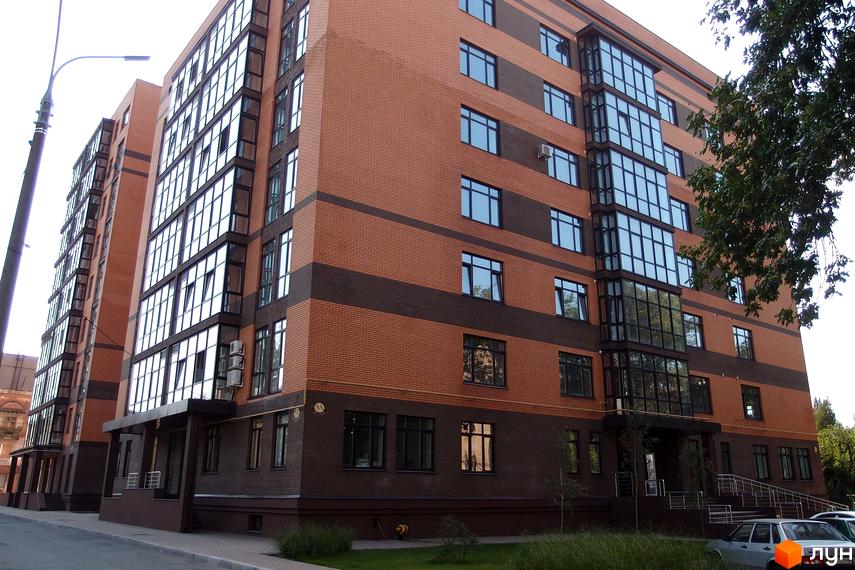 Зовнішній вигляд новобудови ЖК Palladio: цегляний фасад з темними смугами, панорамне скління та кондиціонери. Прибудинкова територія з травою та деревами.