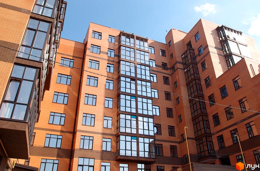 Новобудова ЖК Palladio з цегляним фасадом та великими панорамними вікнами. Будинок має багатоповерхову структуру з виступаючими еркерними елементами.