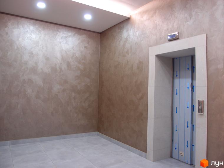 Новобудова Palladio: інтер'єр холу з текстурними стінами та ліфтом. Оздоблення плиткою, декоративною штукатуркою та металевими елементами.
