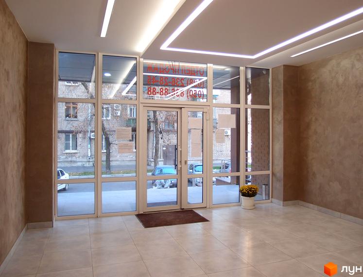 Вхідна група житлового комплексу Palladio з великими вікнами та дверима, що виходять на вулицю. Навколо будівлі розташовані дерева та проїжджа частина.