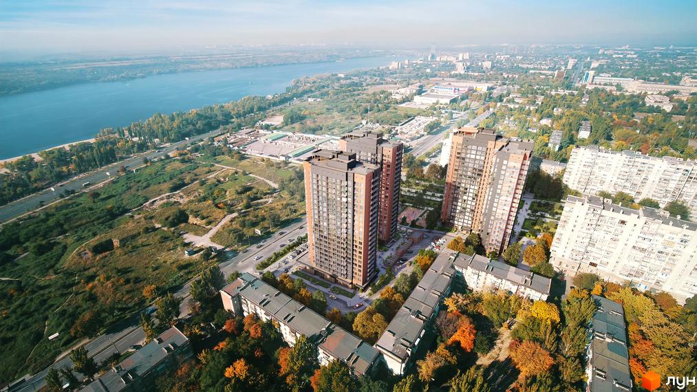 Високі будинки ЖК Central з терасами та панорамними вікнами, поруч зелені насадження та річка. Благоустрій території включає дитячі майданчики та зони відпочинку.