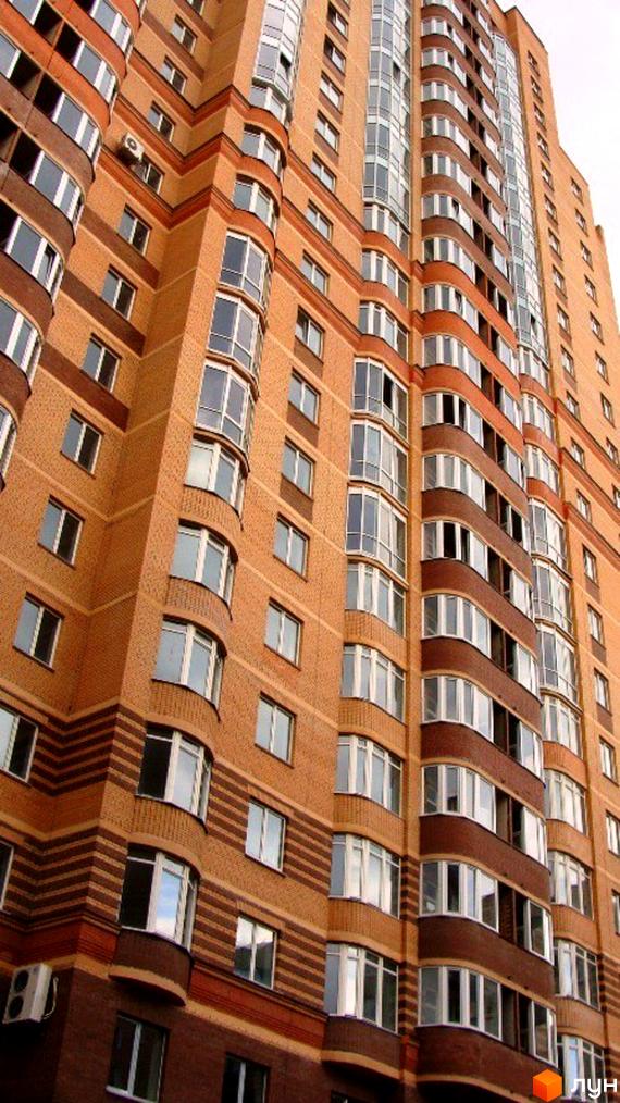 Житловий комплекс на пров. Лабораторний, 6 з фасадом з цегли та великими вікнами. Прибудинкова територія оформлена зеленими насадженнями.