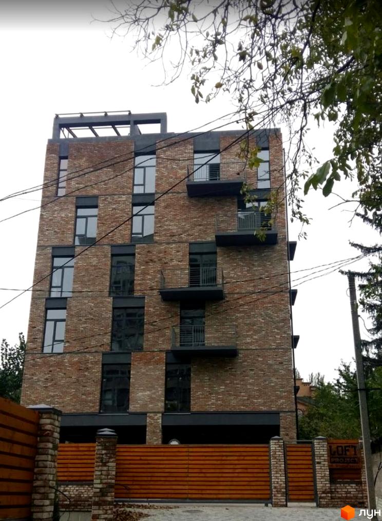 Новобудова з цегляним фасадом, темними вікнами та балконами. Перед будинком дерев'яний паркан, цегляні стовпи та вивіска LOFT PROJECT.