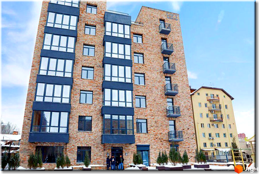 Житловий комплекс LOFT на вул. Шевченка, 25. Цегляний будинок з великими вікнами та балконами, навколо висаджені хвойні дерева.