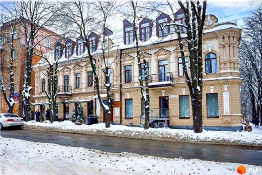 Будівля на пл. Соборна, 6, світлого кольору з класичними елементами та мансардними вікнами. Зимова вулиця із засніженими деревами.