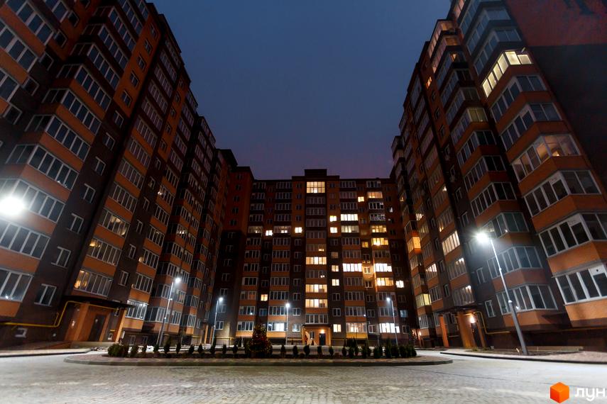 Житловий комплекс Олександрівський 1: будинки з помаранчевими фасадами та освітленими вікнами. Внутрішній двір з бруківкою, ліхтарями та озелененням.