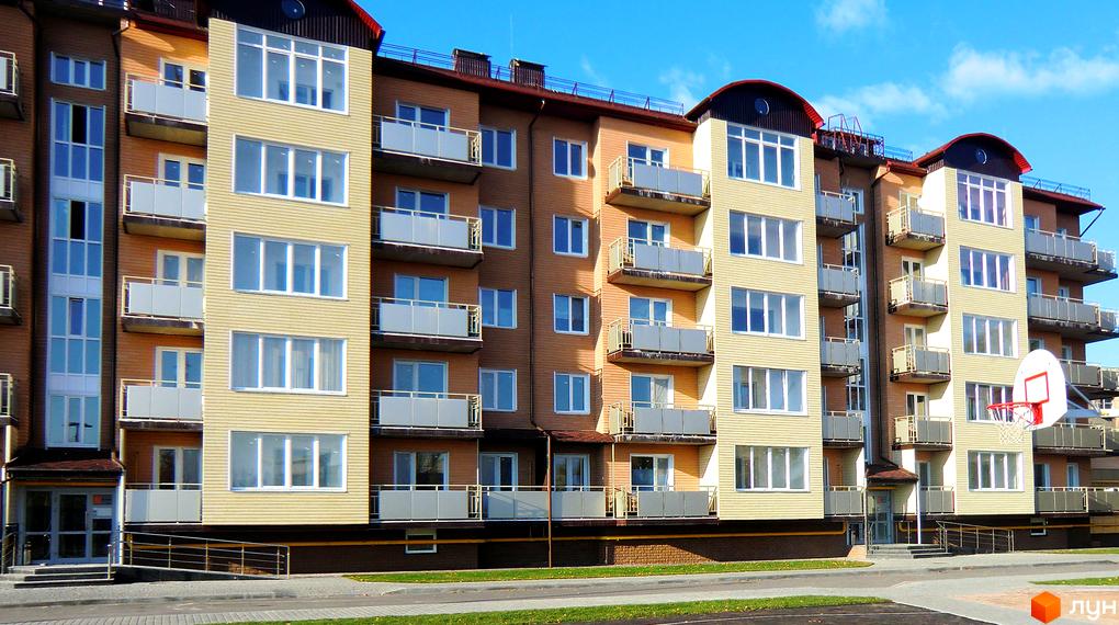 Фасад житлового комплексу Фаворит з балконами та великими вікнами. Поруч розташований дитячий майданчик з баскетбольним кільцем.