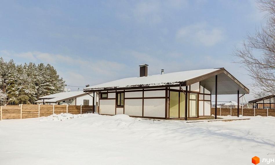 Будинок котеджного містечка Удачино з білими стінами та темними балками, дах покритий снігом. Навколо засніжена територія та ліс.