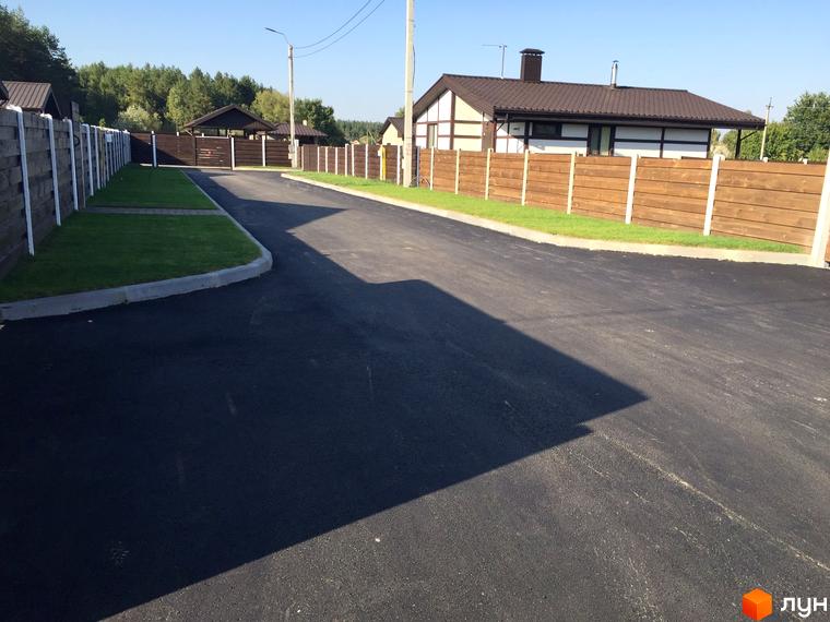 Котеджне містечко Удачино: будинок з коричневим дахом та білими стінами з темними дерев'яними балками, асфальтована дорога та зелені газони.