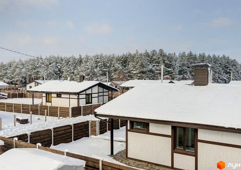 Будинки Котеджного містечка Удачино з білими фасадами, темними балками та засніженими дахами. Навколо дерев'яні паркани та засніжений ліс.