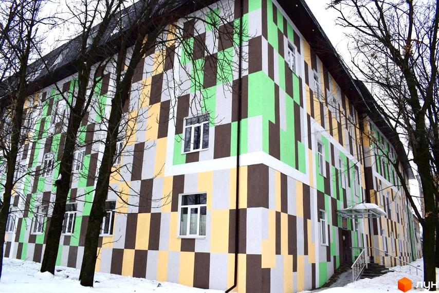 Житловий комплекс Нетеченський з фасадом, оздобленим прямокутними блоками зеленого, коричневого, жовтого та сірого кольорів. Навколо будинку сніг та дерева.