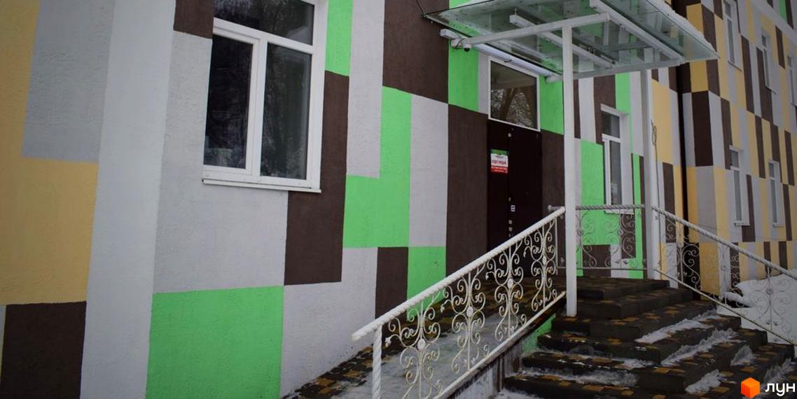 Вхід до Житлового комплексу Нетеченський з фасадом, що має візерунок з різнокольорових блоків. Перед входом розташовані сходи з білими металевими поручнями.